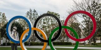 Olympijské hry Tokio sa definitívne presúvajú do roku 2021, povedal vrcholový predstaviteľ MOV Japonka stojaca pri olympíjskych kruhoch v rúške